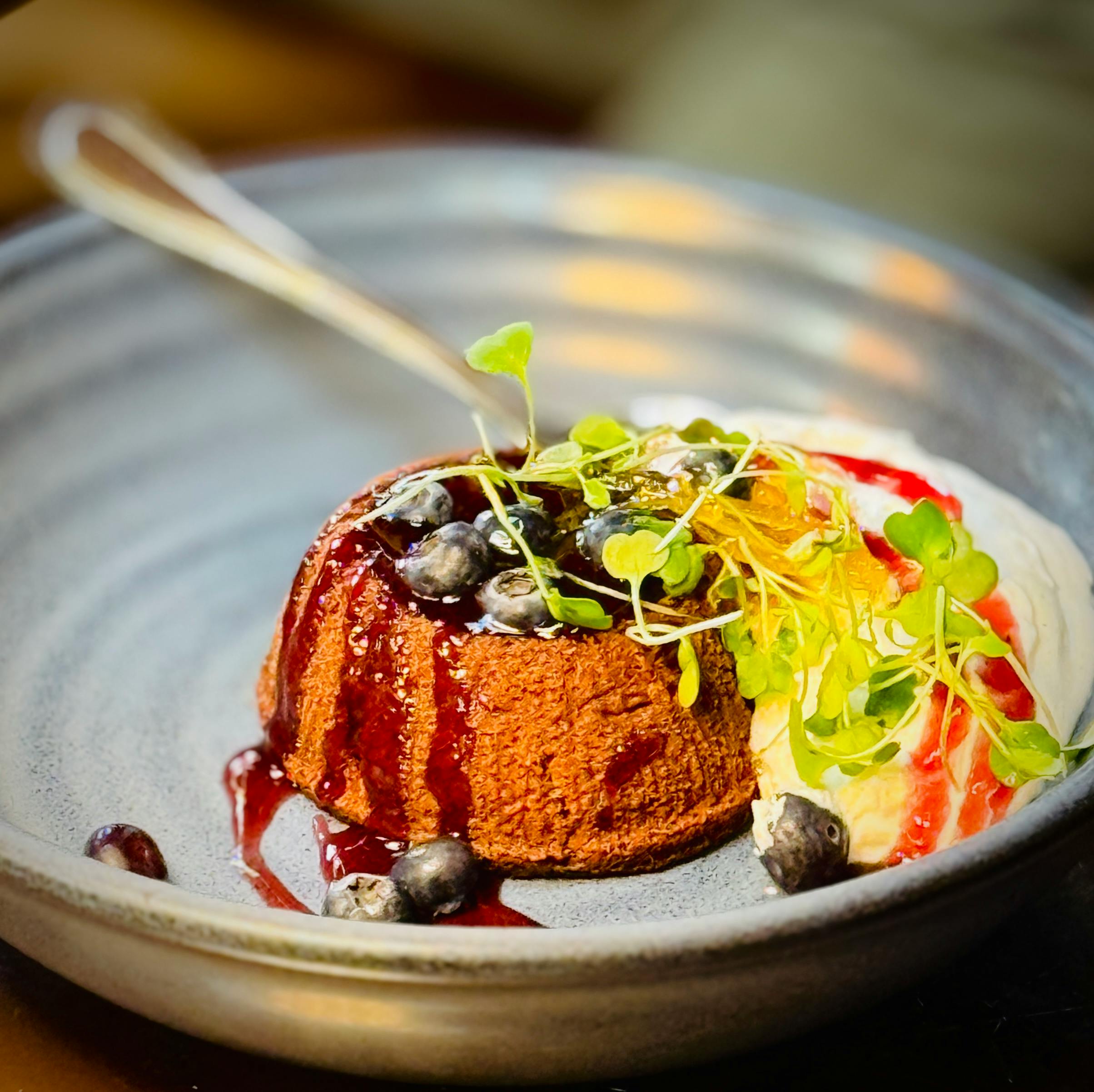 Indulge in a sumptuous chocolate dessert topped with fresh berry sauce and cream, garnished with microgreens.